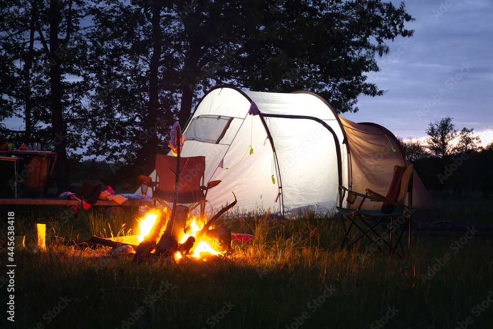 Summer camping. Traveling with a tent. Campfire sunset. Different things and folding chairs near the tent.