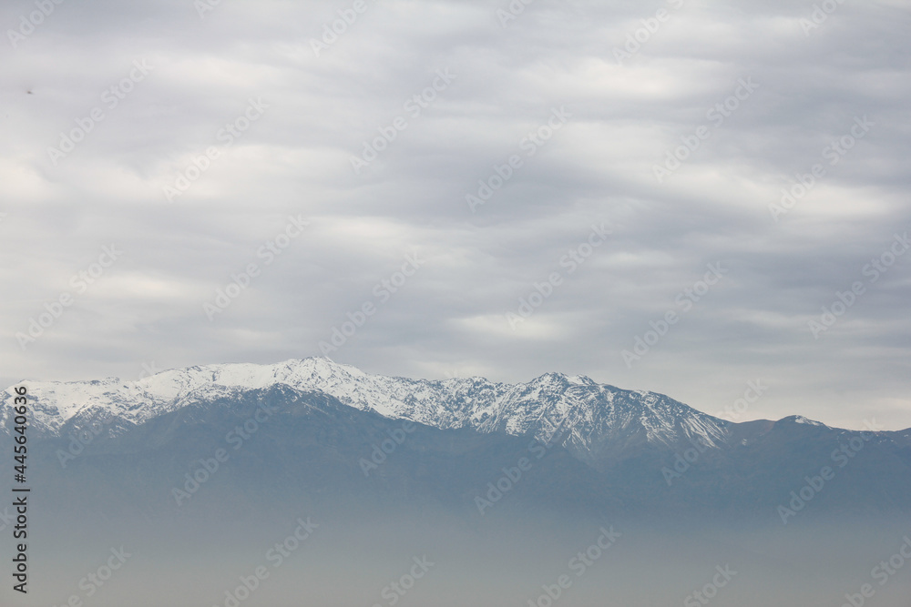 Mountain top covered in snow above the pollution clouds of urban area in Santiago, Chile