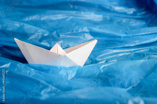 Ship origami of white paper among a blue plastic bag as if on waves of water. Conceptual photo