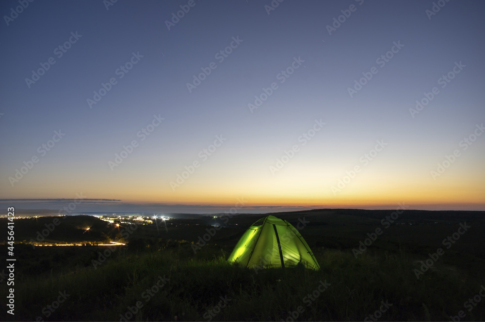 Morning landscape, tent against the background of sunrise and city lights on a hill in Ukraine
