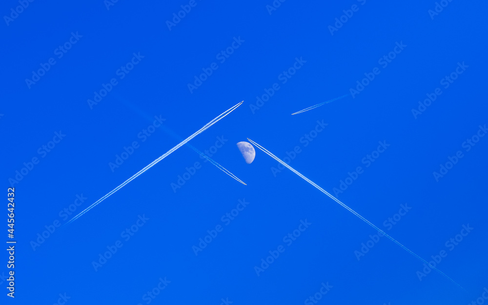 Planes fly, crossing their paths to each other directly under the moon, leaving traces behind on a clear blue sky- the true scene Planes fly, crossing their paths to each other directly under the moon, leaving traces behind on a clear blue sky- the true scene