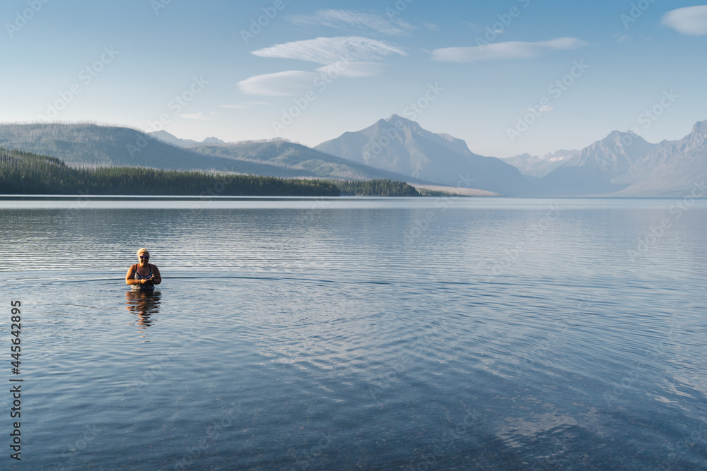 Blonde adult woman enjoys taking a dip in the cold waters of Lake McDonald in Glacier National Park during a heatwave