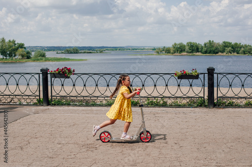 a child quickly rides a scooter along the embankment along the bay, having fun on a family weekend, children's activity. 