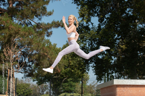 Healthy and fit atrractive blonde woman leaping to the left over obstacles at the park while looking ahead