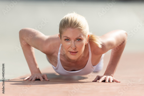 Healthy and fit atrractive blonde woman shows the core and arm strength to hold a push up in lowest position with a relaxed look on her face
