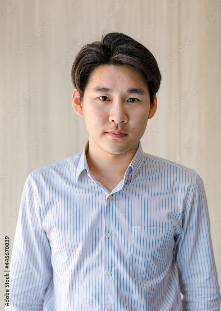 Portrait Close up studio mug shot of young handsome successful Asian male businessman wears green stripe white long sleeve shirt stands look at camera in front brown wooden wallpaper background Portrait Close up studio mug shot of young handsome successful Asian male businessman wears green stripe white long sleeve shirt stands look at camera in front brown wooden wallpaper background