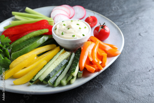 Fresh raw vegetable sticks and sauce on black table, closeup