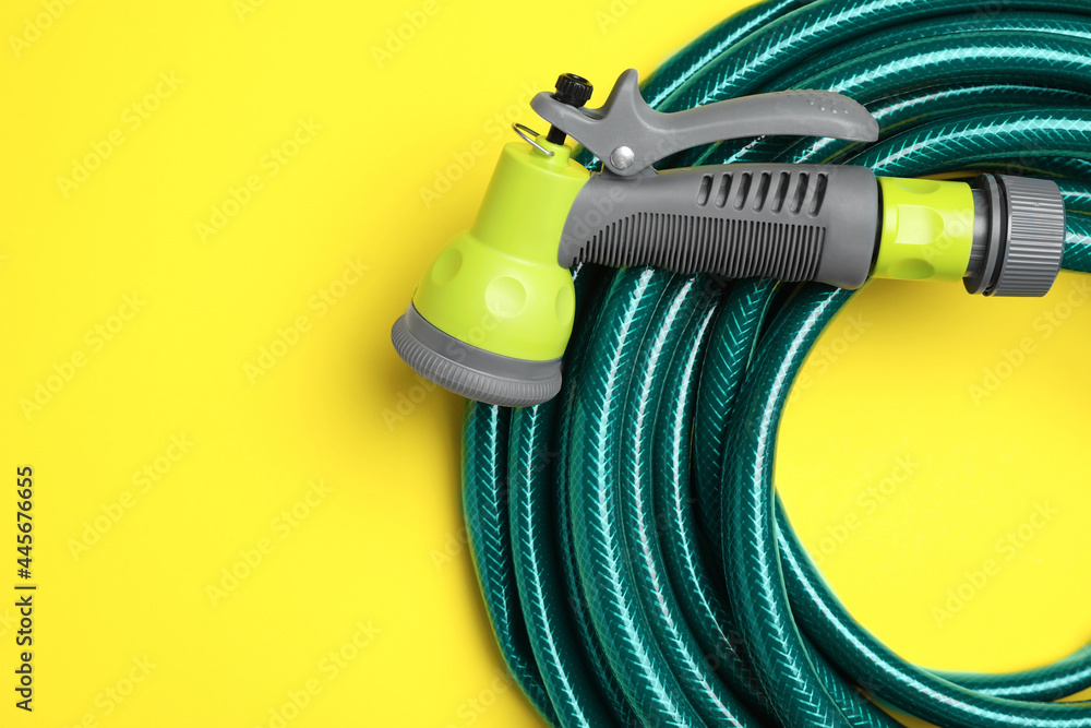 Watering hose with sprinkler on yellow background, top view. Space for text Watering hose with sprinkler on yellow background, top view. Space for text