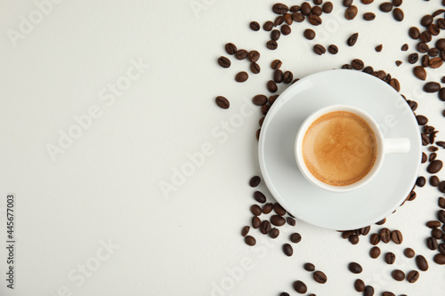 Cup of hot aromatic espresso and roasted beans on white table, flat lay. Space for text