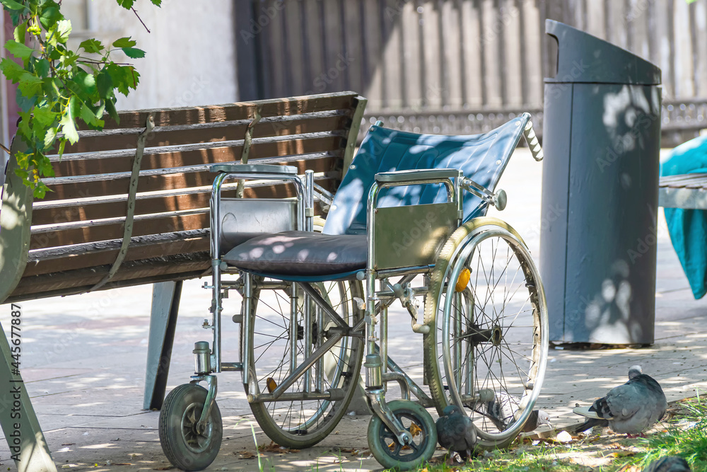 An old wheelchair stands near a bench on the lawn.