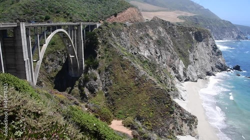 View of Bixby Bridge in Big Sur State Park in California. Vegetation and ocean waves can be seen along the coastline on Highway 1.