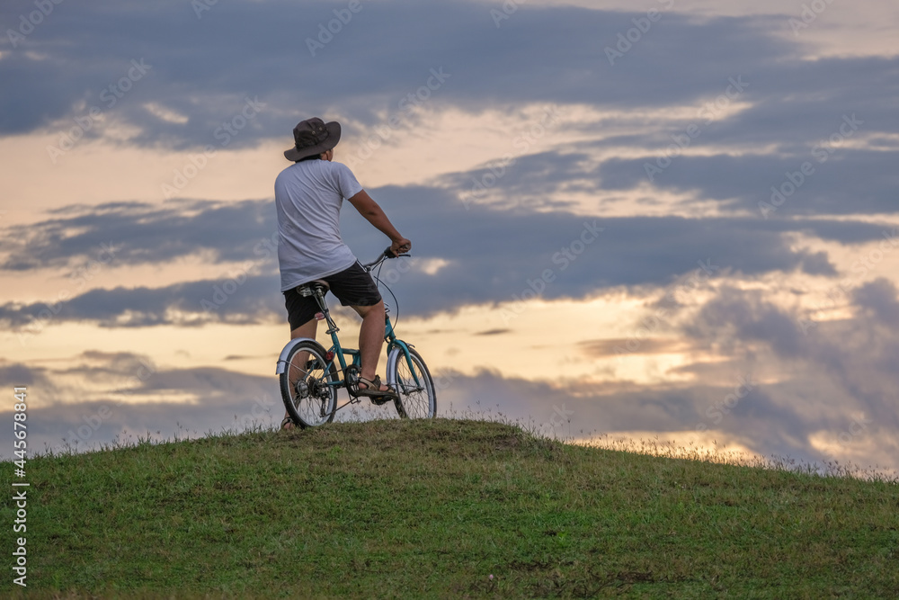 The back of a man driving a bicycle on a green lawn at sunrise