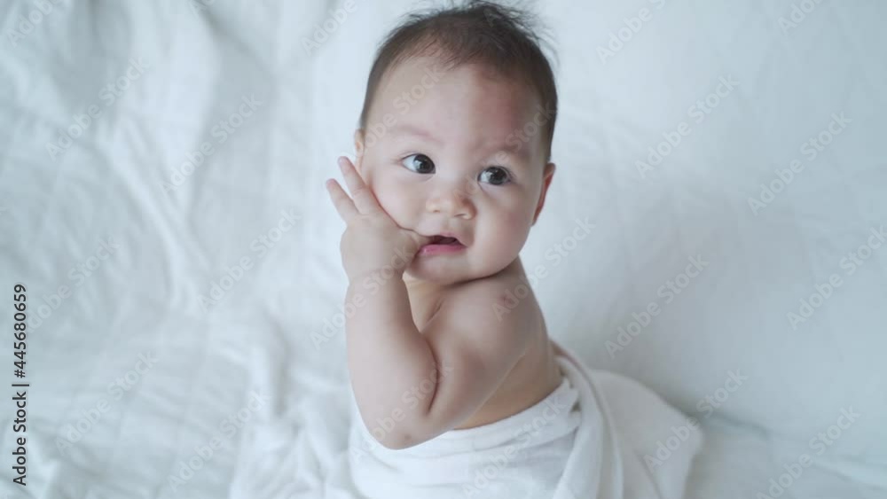 portrait of asian baby infant 6 months old naked after bathing covered with white towel. happy innocence baby kid sitting and crawling on bed. sucking hand age baby portrait copy space provided. portrait of asian baby infant 6 months old naked after bathing covered with white towel. happy innocence baby kid sitting and crawling on bed. sucking hand age baby portrait copy space provided.