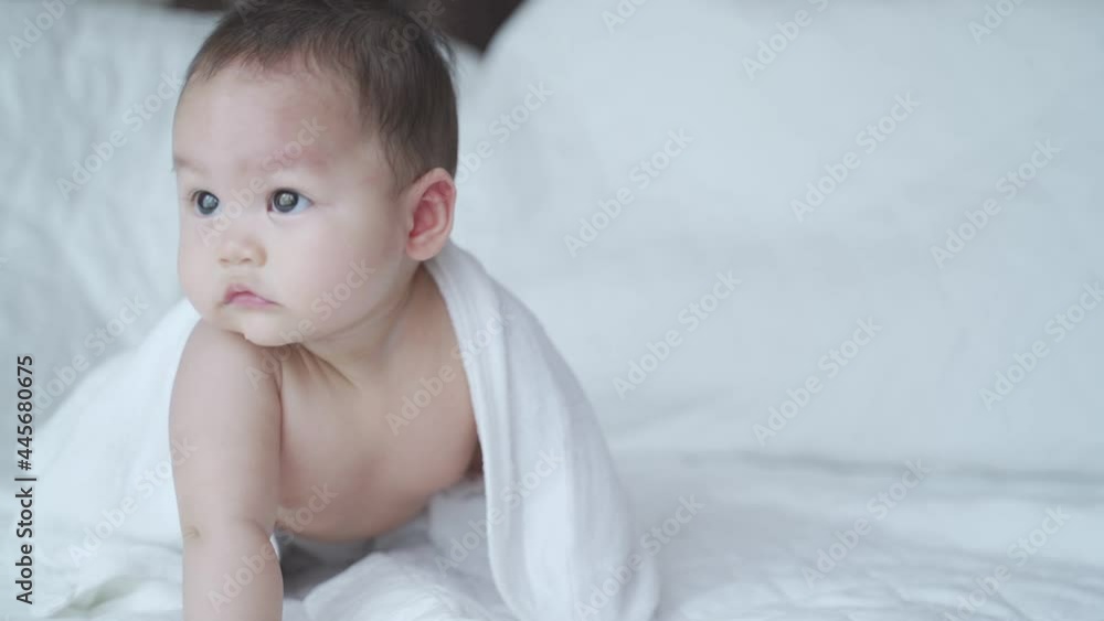 portrait of asian baby infant 6 months old naked after bathing covered with white towel. happy innocence baby kid sitting and crawling on bed. sucking hand age baby portrait copy space provided. portrait of asian baby infant 6 months old naked after bathing covered with white towel. happy innocence baby kid sitting and crawling on bed. sucking hand age baby portrait copy space provided.