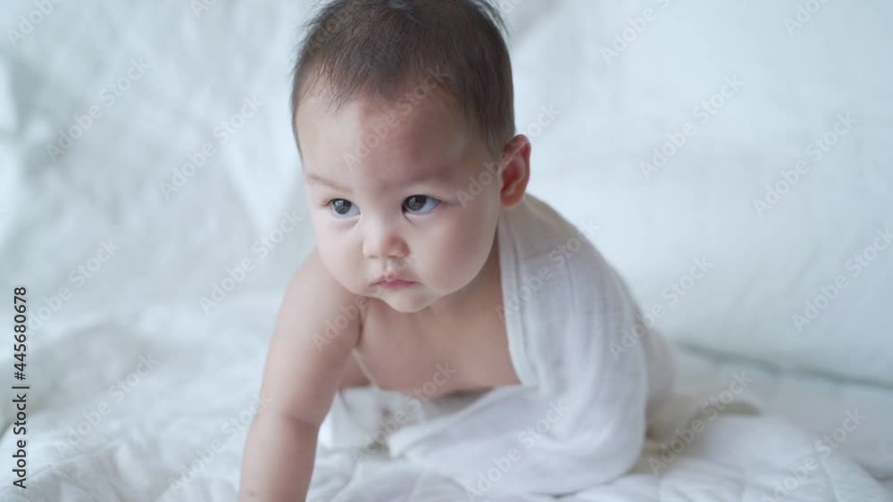 portrait of asian baby infant 6 months old naked after bathing covered with white towel. happy innocence baby kid sitting and crawling on bed. sucking hand age baby portrait copy space provided. portrait of asian baby infant 6 months old naked after bathing covered with white towel. happy innocence baby kid sitting and crawling on bed. sucking hand age baby portrait copy space provided.