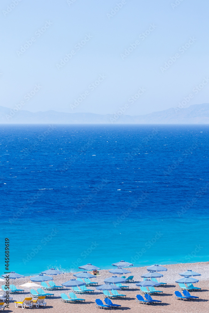Colorful umbrellas and sunbeds on an empty beach resort - vacation concept on Greece islands in Aegean and Mediterranean seas Colorful umbrellas and sunbeds on an empty beach resort - vacation concept on Greece islands in Aegean and Mediterranean seas