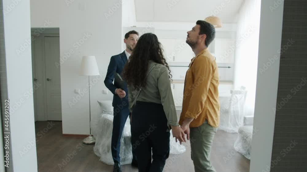Happy real estate agent in suit is showing new house to couple of buyers talking gesturing making property presentation. Business and people concept. Happy real estate agent in suit is showing new house to couple of buyers talking gesturing making property presentation. Business and people concept.