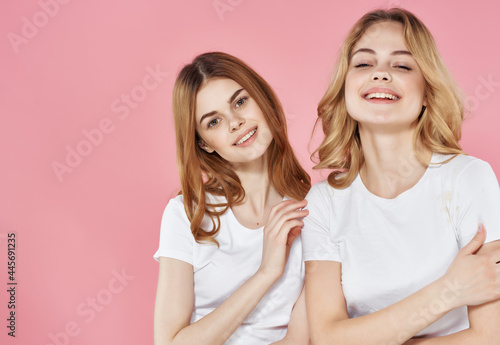 two sisters white t-shirts hug friendship emotions pink background