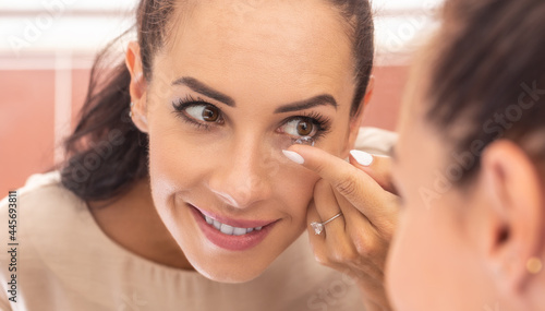 A young woman puts contact lenses in her eyes in the morning in the bathroom in front of a mirror