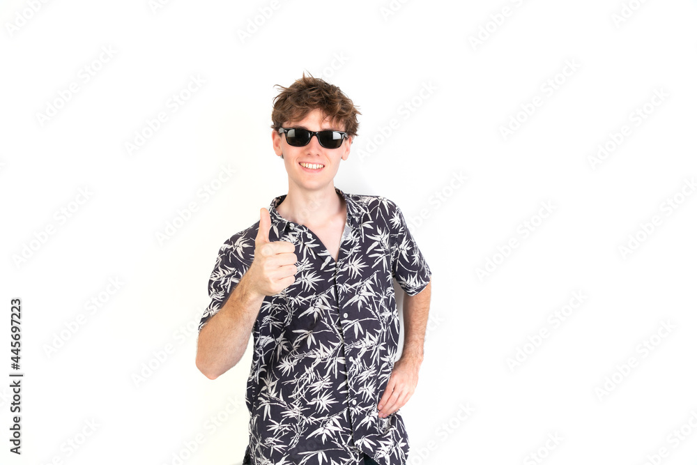 Teenager with thumb up. Wearing sunglasses and palm trees shirt. White background, 18-20 years old. White european guy. Teenager with thumb up. Wearing sunglasses and palm trees shirt. White background, 18-20 years old. White european guy.