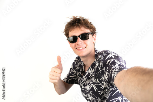 Selfie photo of a teenager with thumb up. Wearing sunglasses and a palm trees shirt. White background, 18-20 years old. White european guy.