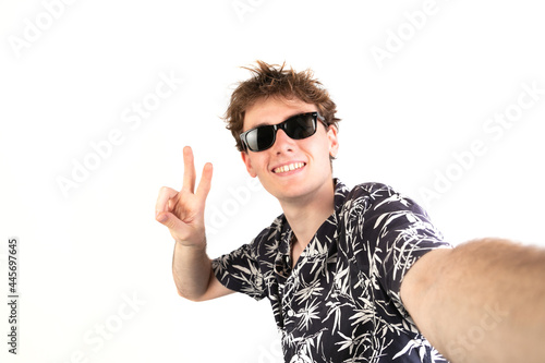 Selfie photo of a teenager raising two fingers doing letter V, victory symbol. Wearing sunglasses and a palm trees shirt. white background, 18-20 years old. White european guy.