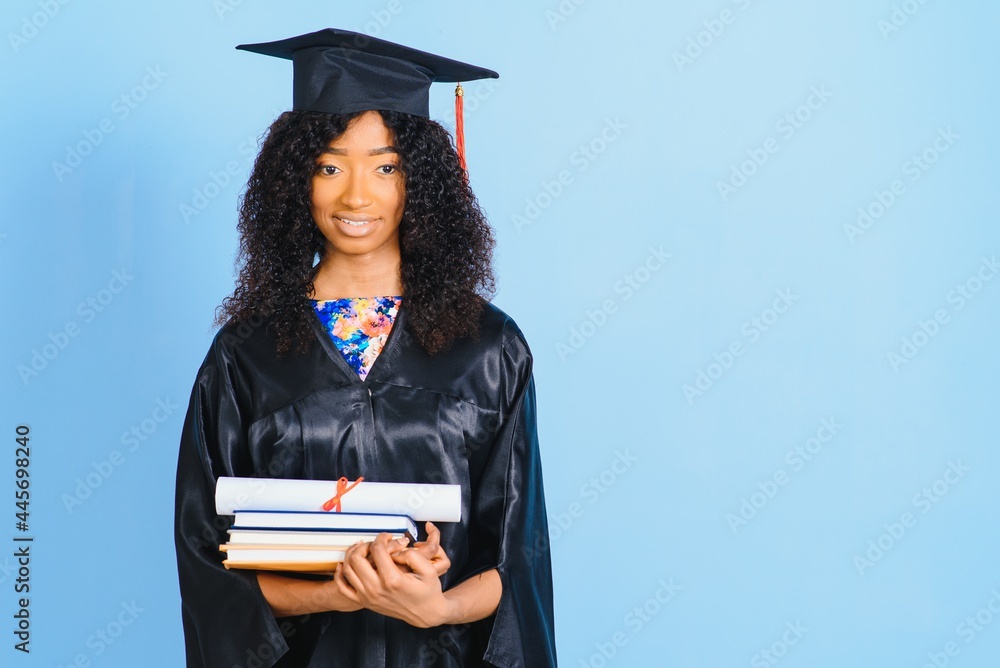 African-American beautiful woman in a black robe and hat, on a blue isolated background smiles. African-American beautiful woman in a black robe and hat, on a blue isolated background smiles.