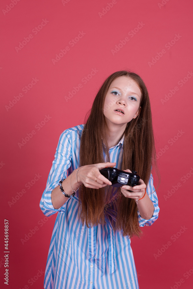 Little kid girl 13 years old in blue dress isolated on pink background holding joystick gaming serious concentrated playing games Little kid girl 13 years old in blue dress isolated on pink background holding joystick gaming serious concentrated playing games