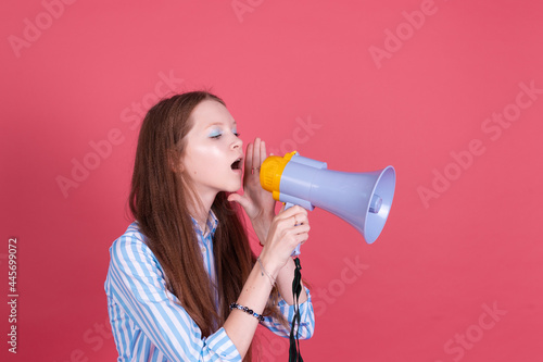 Little kid girl 13 years old in blue dress isolated on pink background whispering in megaphone