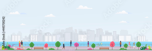 Waterfront with people and view at modern city. Men and women relax in city park with trees, flowers, wooden benches and city buildings on horizon.
