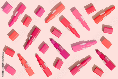 Creative pattern made with red and pink lipsticks of different shades. Summer make up cosmetics concept. Lipstick on pink background in pop art style. Open lipstick tubes and caps.