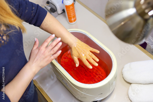 Paraffin theoraphy. Female hand and orange paraffin wax in bowl. Manicure and skincare. Woman girl in beauty spa salon.