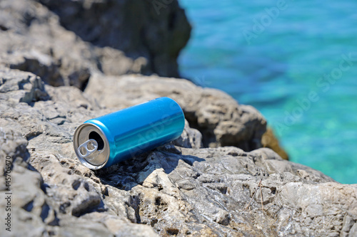 blue aluminum beverage can left behind on stone coast on mediterriean, problem of marine pollution of inconsiderate people