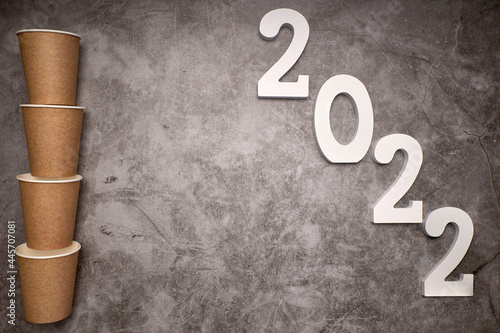 Wooden number 2022 next to recyclable cardboard cups on a dark gray cement background. New Year and Christmas concept