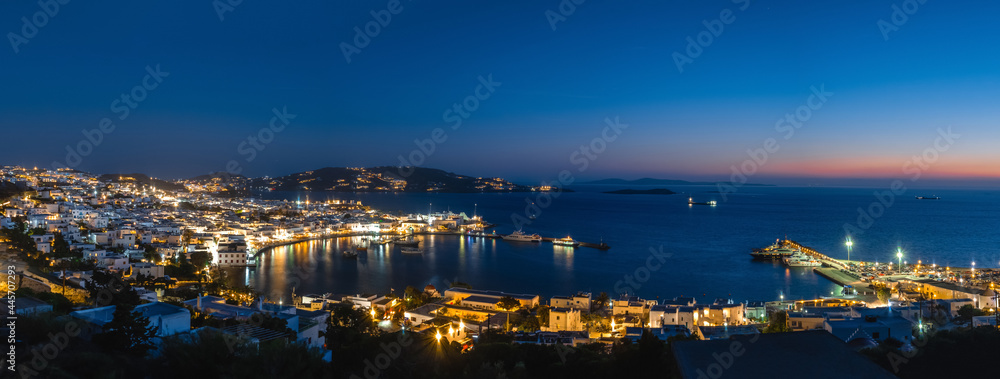 Beautiful night panorama of Mykonos, Greece, ships, port, whitewashed houses. Town lights up. Vacations, leisure, nightlife, Mediterranean lifestyle