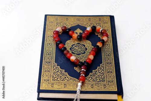 The Quran also romanized Qur'an or Koran is the central religious text of Islam, believed by Muslims to be a revelation from God (Allah), isolated on white background with a heart shaped rosary on it photo