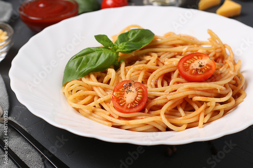 Spaghetti with tomato sauce and cherry tomatoes with basil on white plate on dark background. Closeup