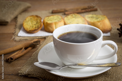 Cup of black coffee with garlic bread on wooden table,