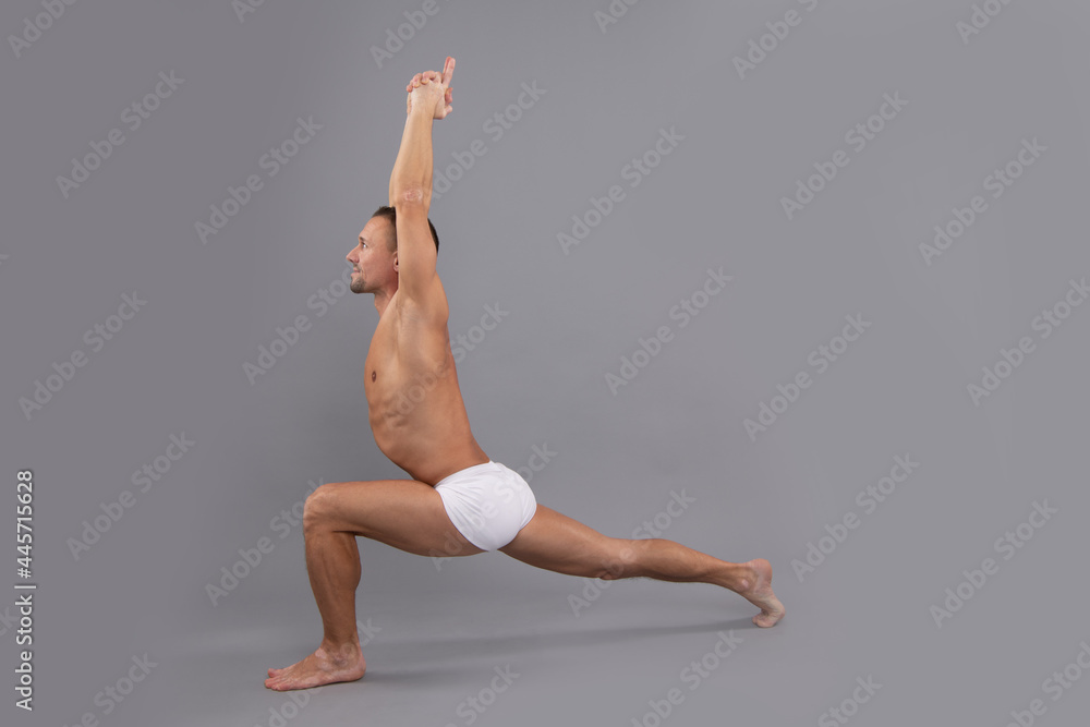 Pilates for every body. Fit guy do crescent lunge greybackground. Yoga and pilates exercise Pilates for every body. Fit guy do crescent lunge greybackground. Yoga and pilates exercise