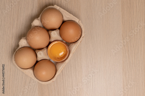 Eggs in eco egg box and whisk on yellow background. Flat lay. Top view. Copy space.