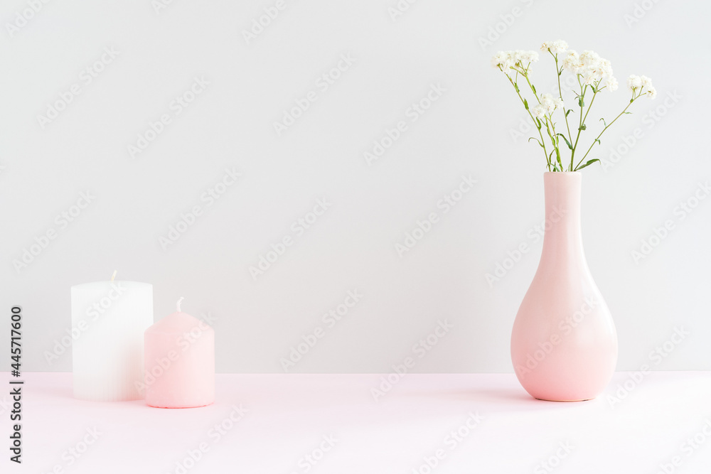 Pink vase with gypsophila and two candles on a pink table with copy space