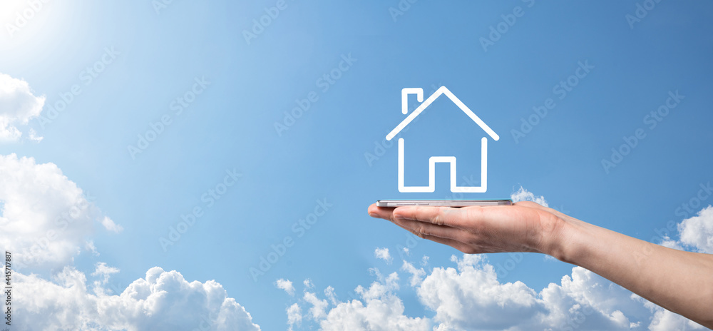 Naklejka premium Male hand holding house icon on blue background. Property insurance and security concept.Real estate concept.Banner with copy space.