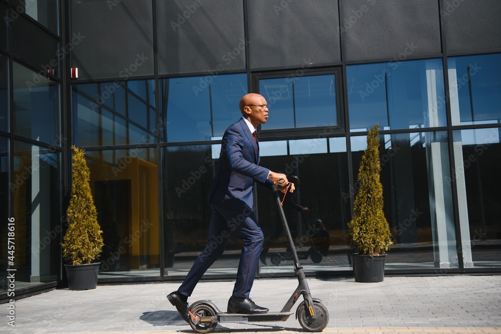 Handsome african 30s man wearing coat smiling while riding electric scooter outdoors Handsome african 30s man wearing coat smiling while riding electric scooter outdoors