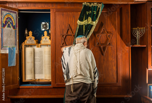 an older jewish man in front of  a bible scroll in a synagogue