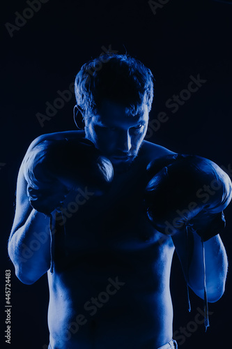 Mixed martial arts fighter in gloves in neon blue. Male portrait of a boxer on a dark background. © SerPak