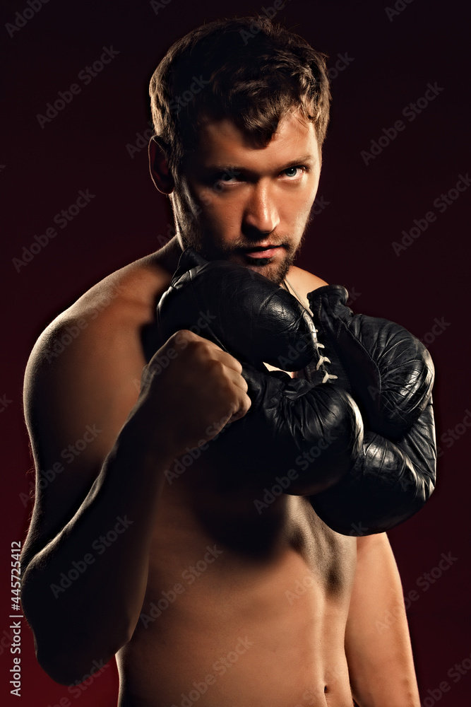 Portrait of a confident fighter on a dark background with a straight and bold look. Silhouette of a boxer with gloves around his neck. Caucasian fighter with a naked torso.
