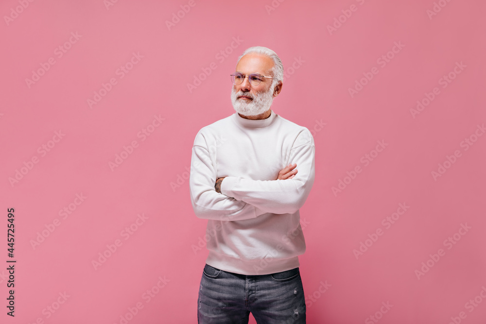 Man in eyeglasses and sweater posing on isolated background. Charming guy with grey hair in cool sweatshirt and jeans looking away.. Man in eyeglasses and sweater posing on isolated background. Charming guy with grey hair in cool sweatshirt and jeans looking away..