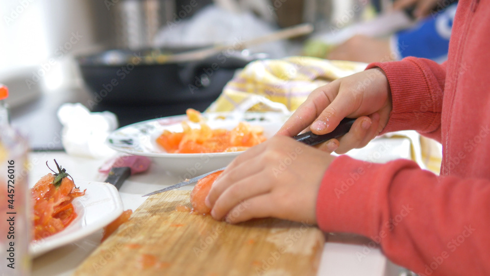 Close-up of children's hands cutting tomatoes. Concept of family cooking. Selective focus.