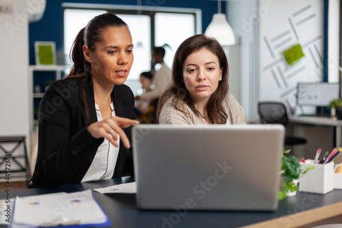 Close up of diverse businesswomen checking graphs from laptop making new strategy for start up business. Manager explaining to colleagues new financial project sitting at desk in startup office