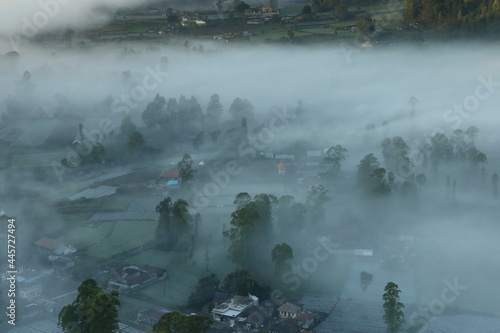 fog covers a village in the valley of mount batur kintamani bali aerial view